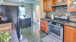 Una cocina con un refrigerador de acero inoxidable, estufa, armarios de madera y salpicadero de azulejos.