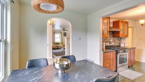 Un comedor con una mesa de mármol, sillas negras y un bol de plata. Se ve una cocina con armarios de madera y una estufa.