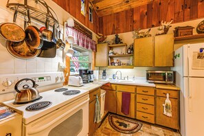 Eine Küche mit Herd, Mikrowelle, Kühlschrank, Holzschränken und einem Fenster mit Blick.