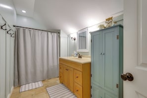 Une salle de bain avec un rideau de douche, un lavabo avec un miroir, des meubles en bois et une porte avec une poignée.
