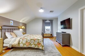 A bedroom with a bed, bedside tables, a dresser, a TV, and a window with curtains.