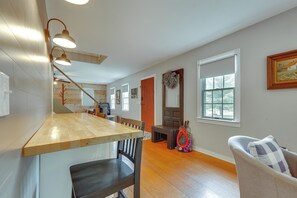 A spacious room with a wooden floor, a dining area with a wooden table and chairs, a large window, and a painting on the wall. - Barn House w/ Private Pond & Dock in Southbury! (Southbury)