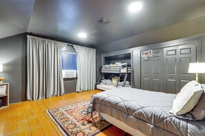 A bedroom with a bed, a window with curtains, a shelf with items, and a door with a basketball hoop.
