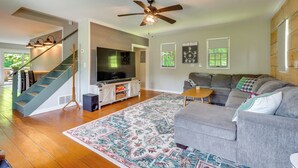 A living room with a grey sofa, a patterned rug, a ceiling fan, and a staircase. - Guest House w/ Private Pond & Dock in Southbury! (Southbury)