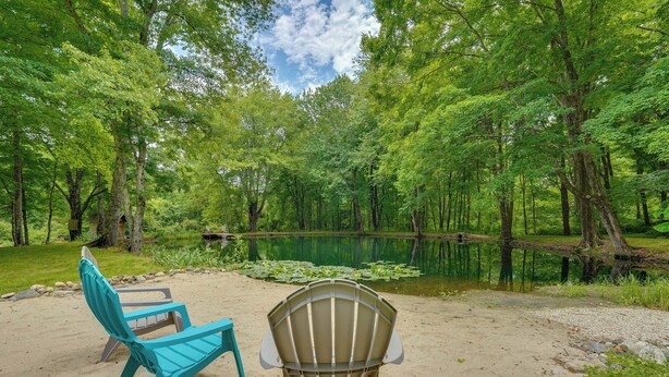A campsite with two chairs, a sandy ground, and a pond surrounded by trees. - Guest House w/ Private Pond & Dock in Southbury! (Southbury)