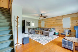 A living room with a sofa set, a coffee table, a wooden floor, a ceiling fan, and a staircase.
