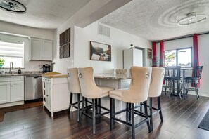 A modern kitchen with white cabinetry, a dining area with bar stools, and a large window with red curtains. - Private Dock & Boat Slip! Belleville Lake Escape (Belleville)