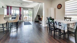 Een eetruimte met een tafel bedekt met een krant, een dartbord aan de muur en een trap die naar een andere kamer leidt.