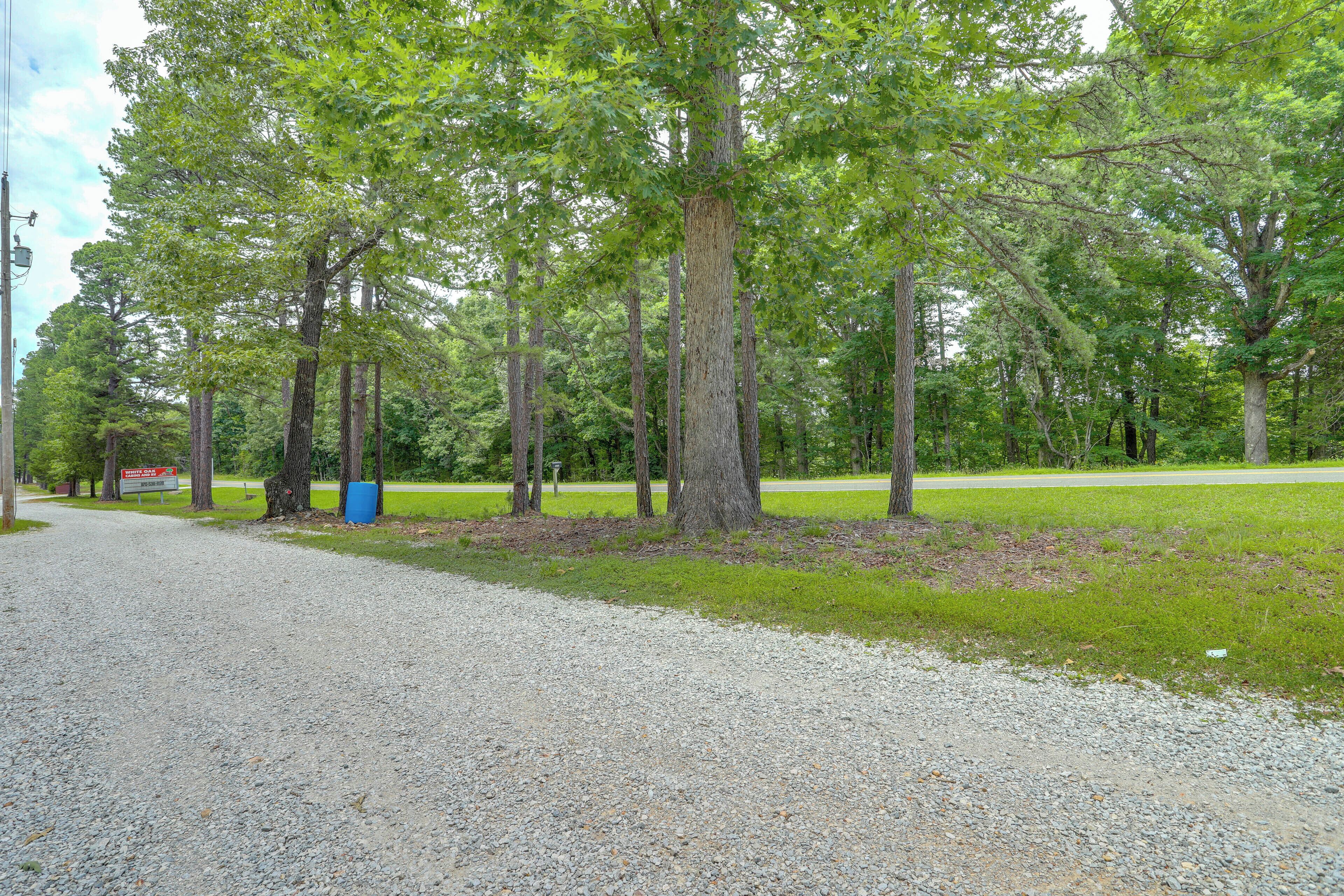 A gravel path leading through a wooded area with trees and a sign in the distance.