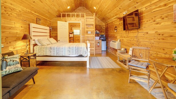 A wooden cabin interior with a bed, a desk, a chair, a television, and a kitchenette. - Near Trails! Ozark Mtn Hideaway w/ Fire Pit, Grill (Fifty-Six)