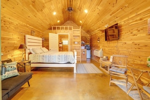 A wooden cabin interior with a bed, a desk, a chair, a television, and a kitchenette.