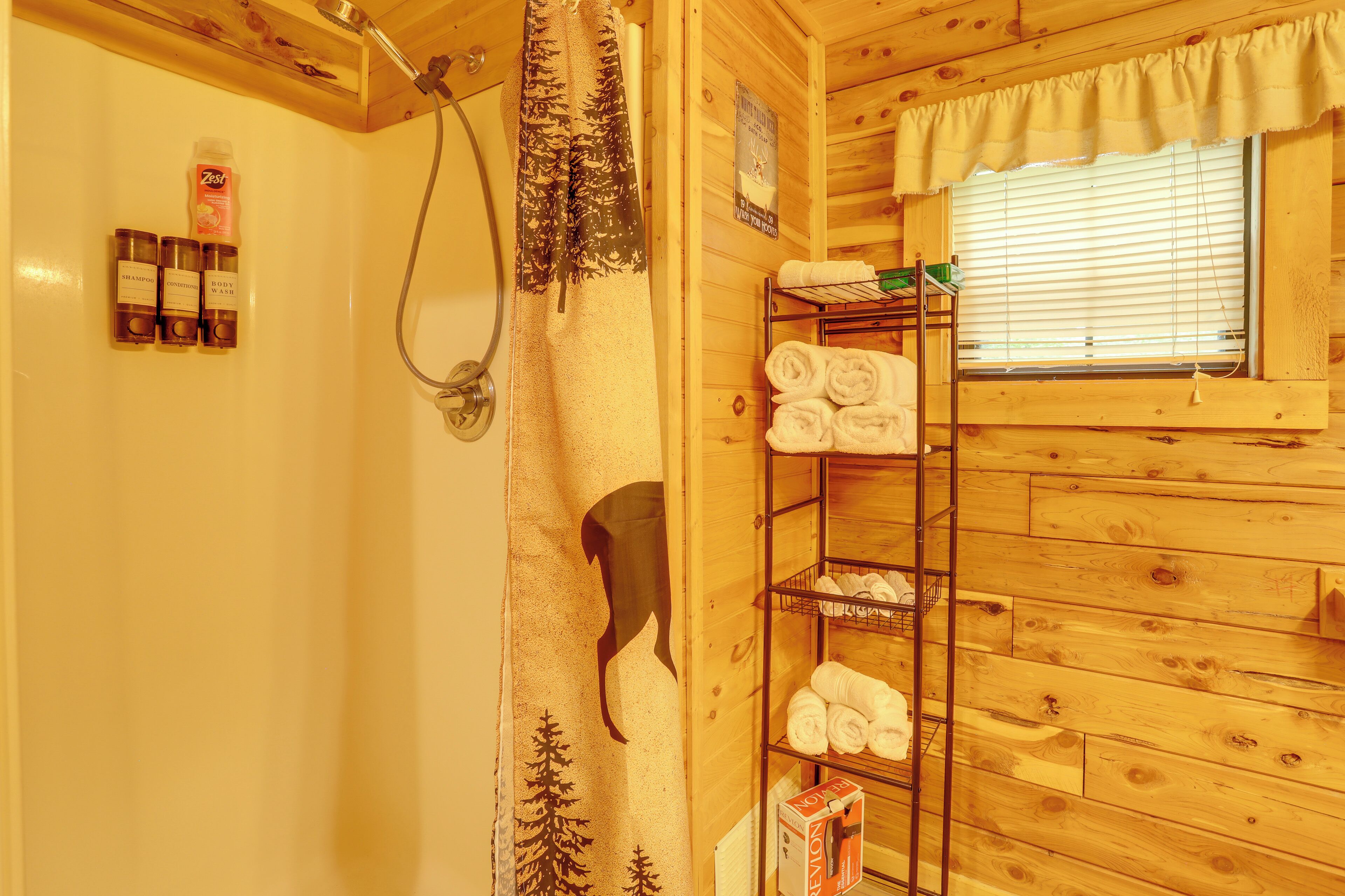 A wooden cabin bathroom with a shower, a towel rack, and a shelf with neatly folded towels.
