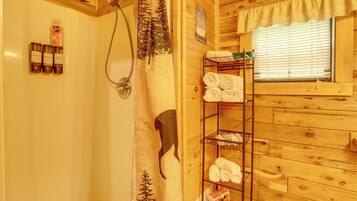 A wooden cabin bathroom with a shower, a towel rack, and a shelf with neatly folded towels.