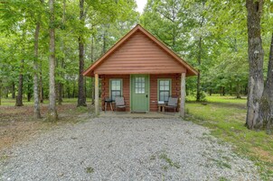 A log cabin with a green door, two windows, and two chairs outside.