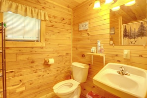 Ein Badezimmer einer Holzhütte mit Toilette, Waschbecken und einem Fenster mit Jalousien.