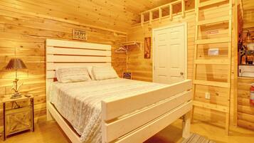 A wooden cabin-style room with a bed, a nightstand, a lamp, a coat rack, and a door with a 'NO SMOKING' sign.