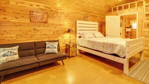 A wooden cabin interior with a bed, sofa, and a small table with a lamp. - Near Trails! Ozark Mtn Hideaway w/ Fire Pit, Grill (Fifty-Six)