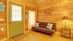 A wooden interior with a green door, a sofa with decorative pillows, a lamp on a side table, and a wall-mounted sign. - Near Trails! Ozark Mtn Hideaway w/ Fire Pit, Grill (Fifty-Six)