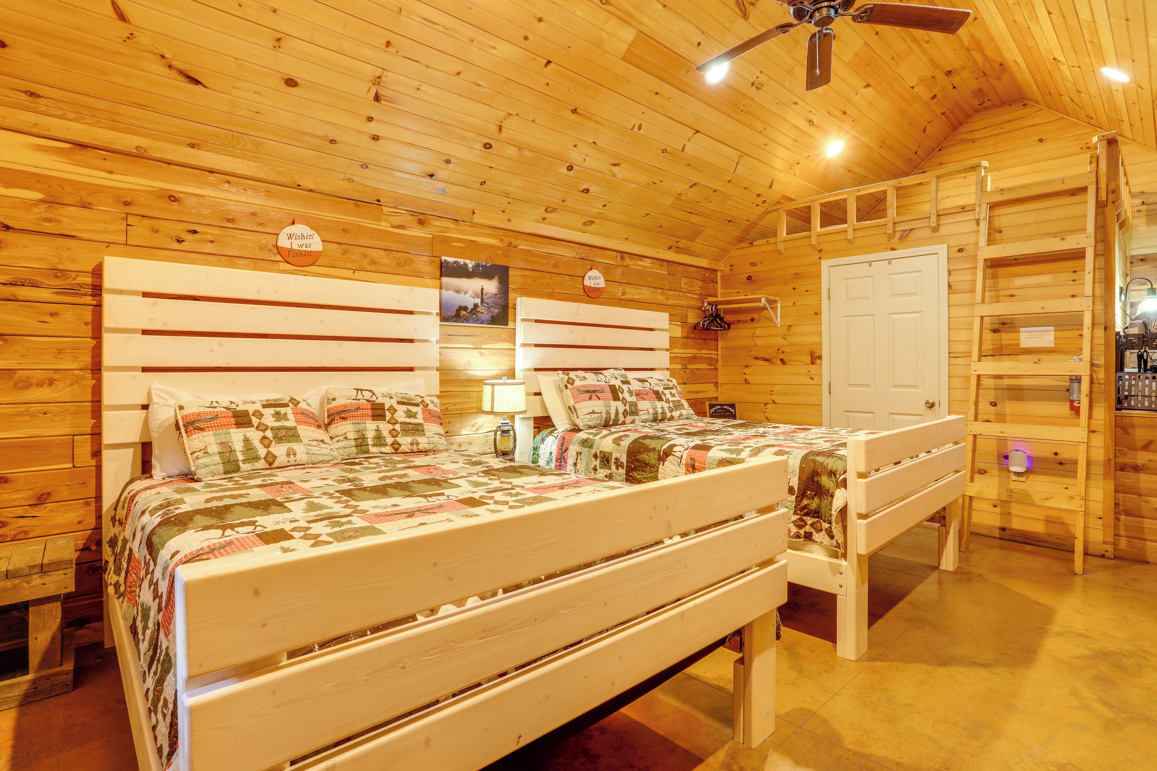A wooden cabin bedroom with a bed, a bench, a ceiling fan, and a door.