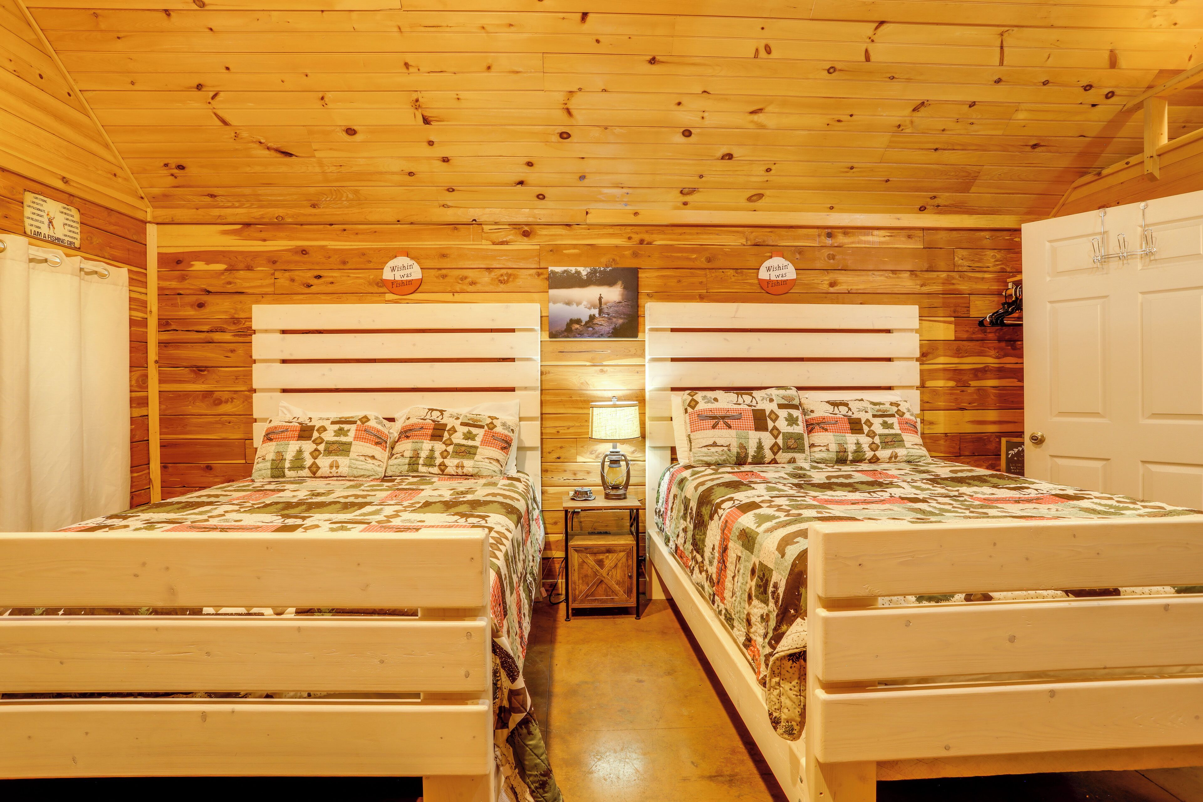 A cabin-style room with two wooden beds, a wooden ceiling, and a small table with a lamp.