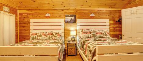 A cabin-style room with two wooden beds, a wooden ceiling, and a small table with a lamp.