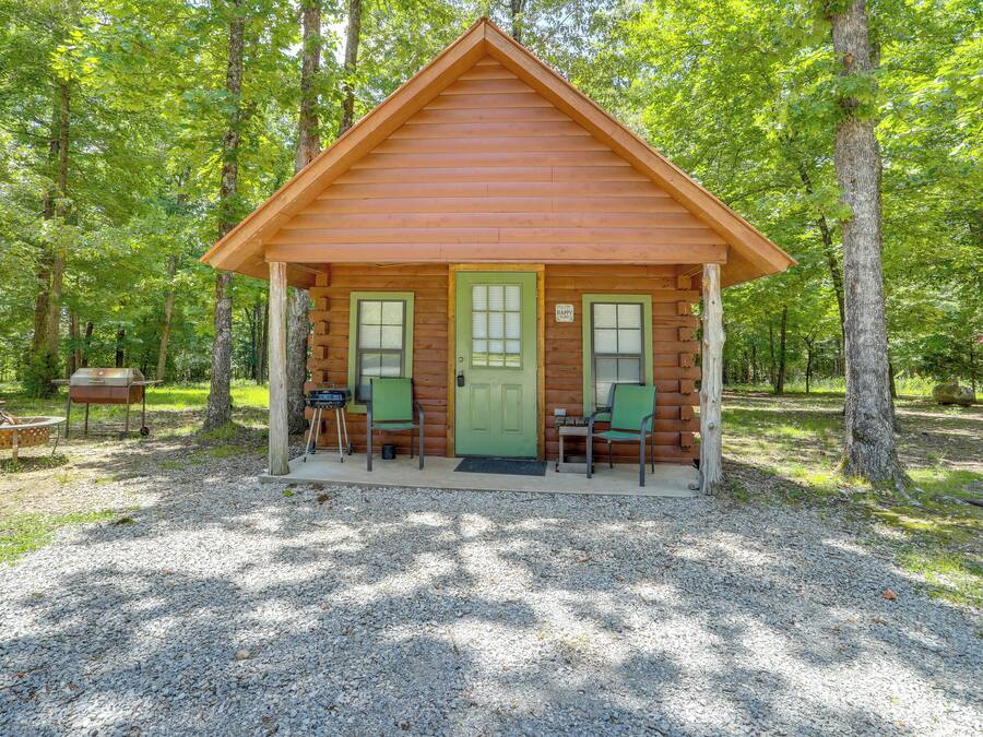 A small log cabin with a green door, two windows, and a porch with chairs.