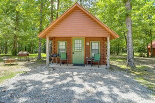 A small log cabin with a green door, two windows, and a porch with chairs.