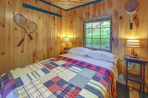 A wooden room with a bed, two tennis rackets, a window, and two wall-mounted lamps. - Waterfront Sand Pond Cabin w/ Views & Fire Pit (Litchfield)
