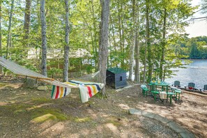 Un hamac, une petite cabane et une table avec des chaises près d’un lac.