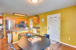 A modern kitchen with a refrigerator, microwave, and oven, a dining area with a round table, and a yellow wall. - Pet-friendly Home w/ Private Yard Near Pittsburgh (Clairton)