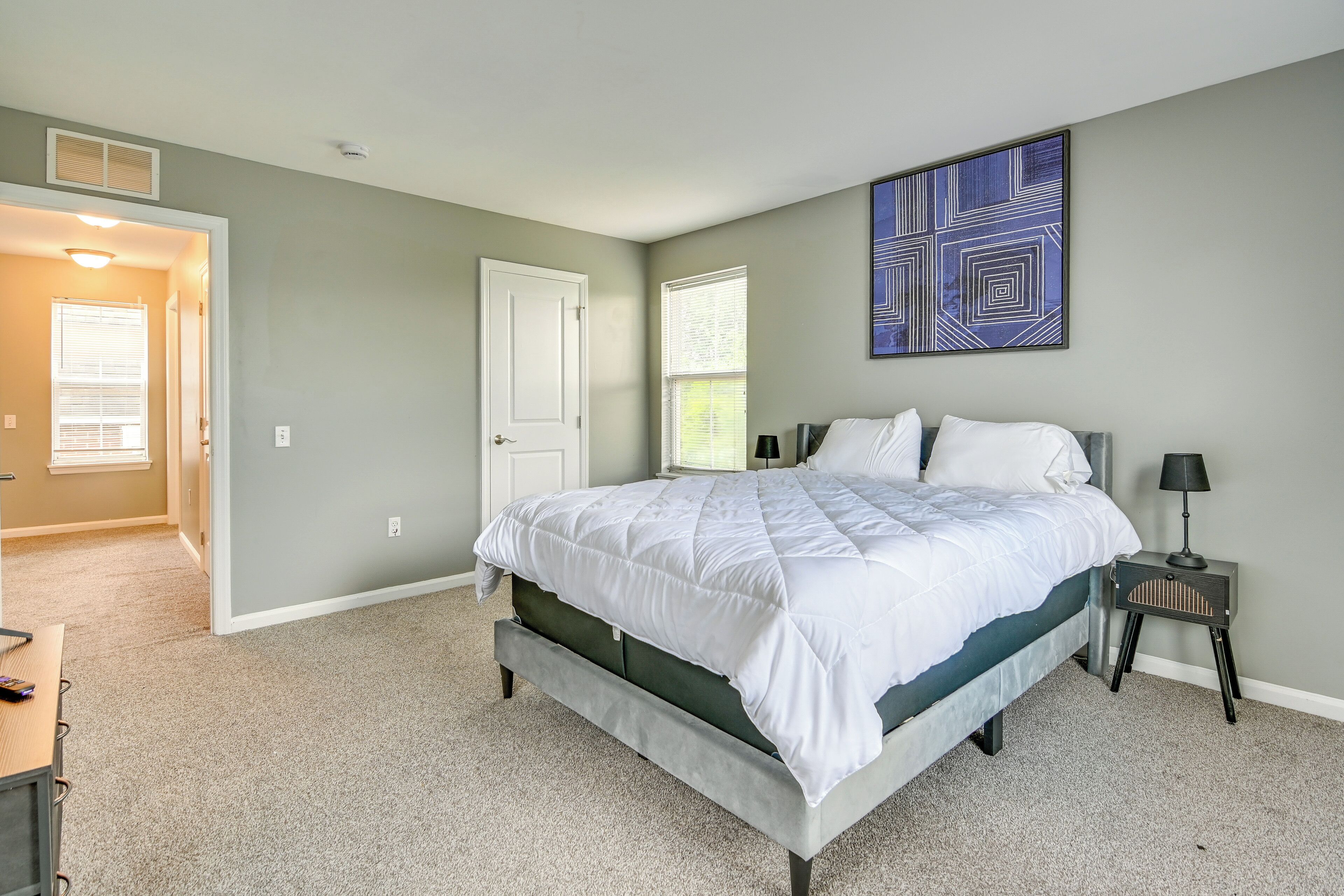 A bedroom with a bed, a nightstand, a wall art piece, and a door leading to another room.