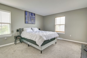 A bedroom with a bed, a nightstand, a wall art piece, and two windows. - Pet-friendly Home w/ Private Yard Near Pittsburgh (Clairton)