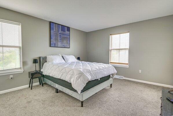A bedroom with a bed, a nightstand, a wall art piece, and two windows.