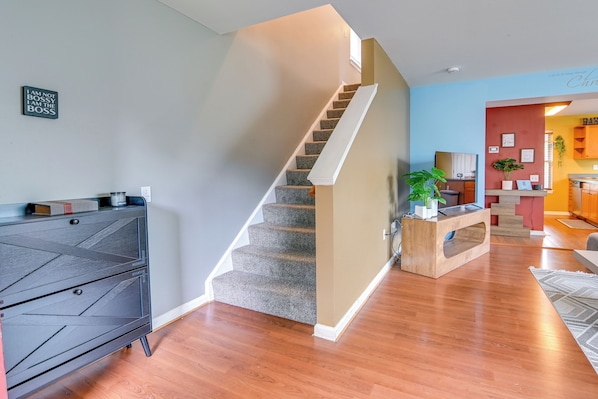 A staircase leading to a second floor, a dark wooden dresser, and a kitchen area with wooden cabinets and a red accent wall. - Pet-friendly Home w/ Private Yard Near Pittsburgh (Clairton)