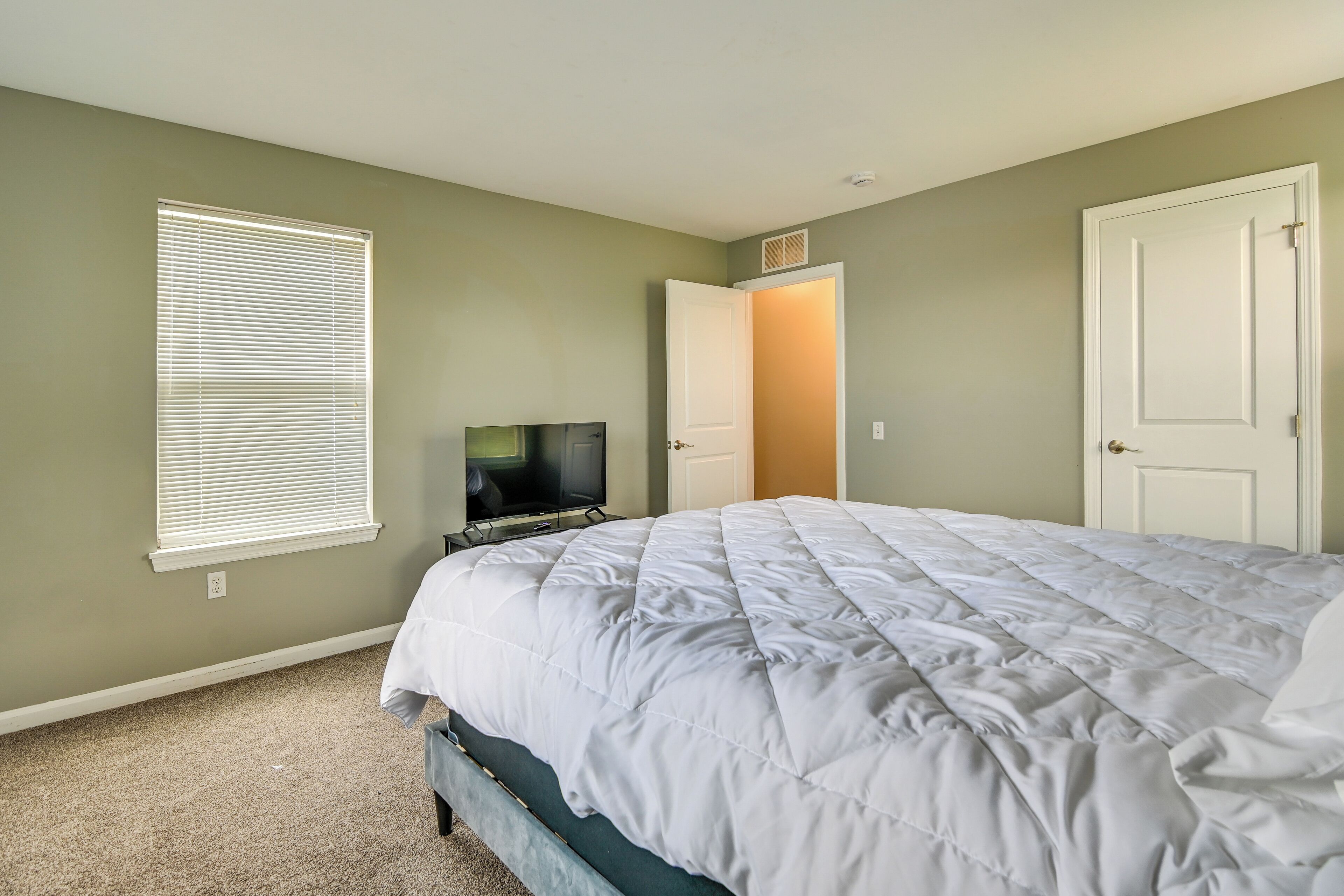 Un dormitorio con una cama, televisión, puerta y ventana con persianas.