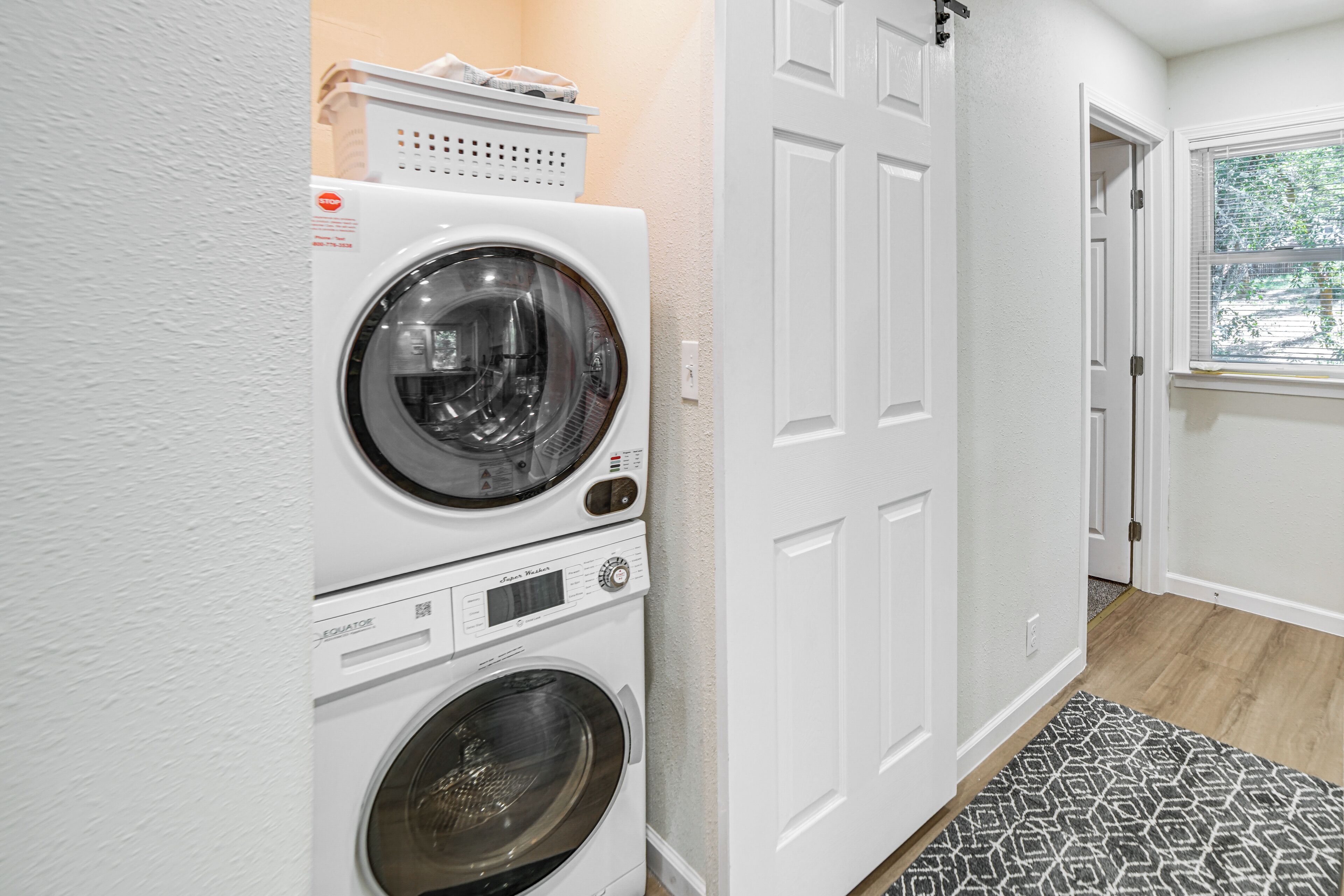 A laundry area with two stacked front-loading washing machines, a white door, and a patterned rug.