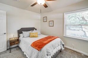 A bedroom with a bed, a nightstand, a ceiling fan, a window, and a door. - Walk to Main St! Quiet Mendocino County Retreat (Willits)