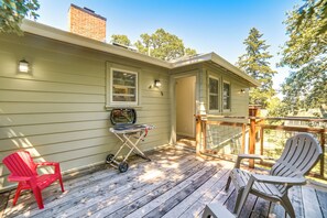 Eine Holzterrasse mit zwei Adirondack-Stühlen, einem Grill und einem kleinen Tisch.