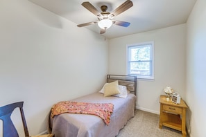 A bedroom with a bed, a ceiling fan, a window, and a nightstand.