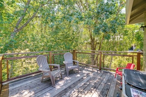 A wooden deck with Adirondack chairs and a grill.