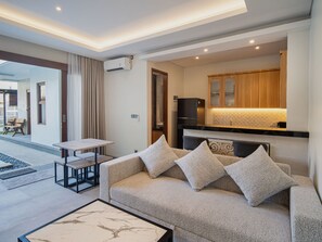 A modern living room with a sofa, a small table, and a kitchen area with wooden cabinets. - Villa RL Sanur (Sanur)
