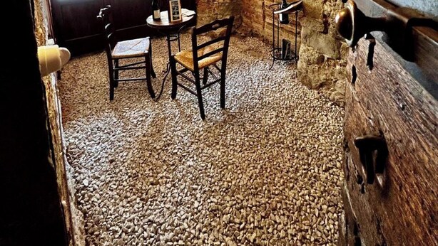 Un interior rústico con paredes de ladrillo visto, vigas de madera, una mesa con sillas y una ventana que da a coches estacionados.