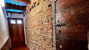 Un pasillo estrecho con pared de ladrillo, puerta de madera y suelo de baldosas.