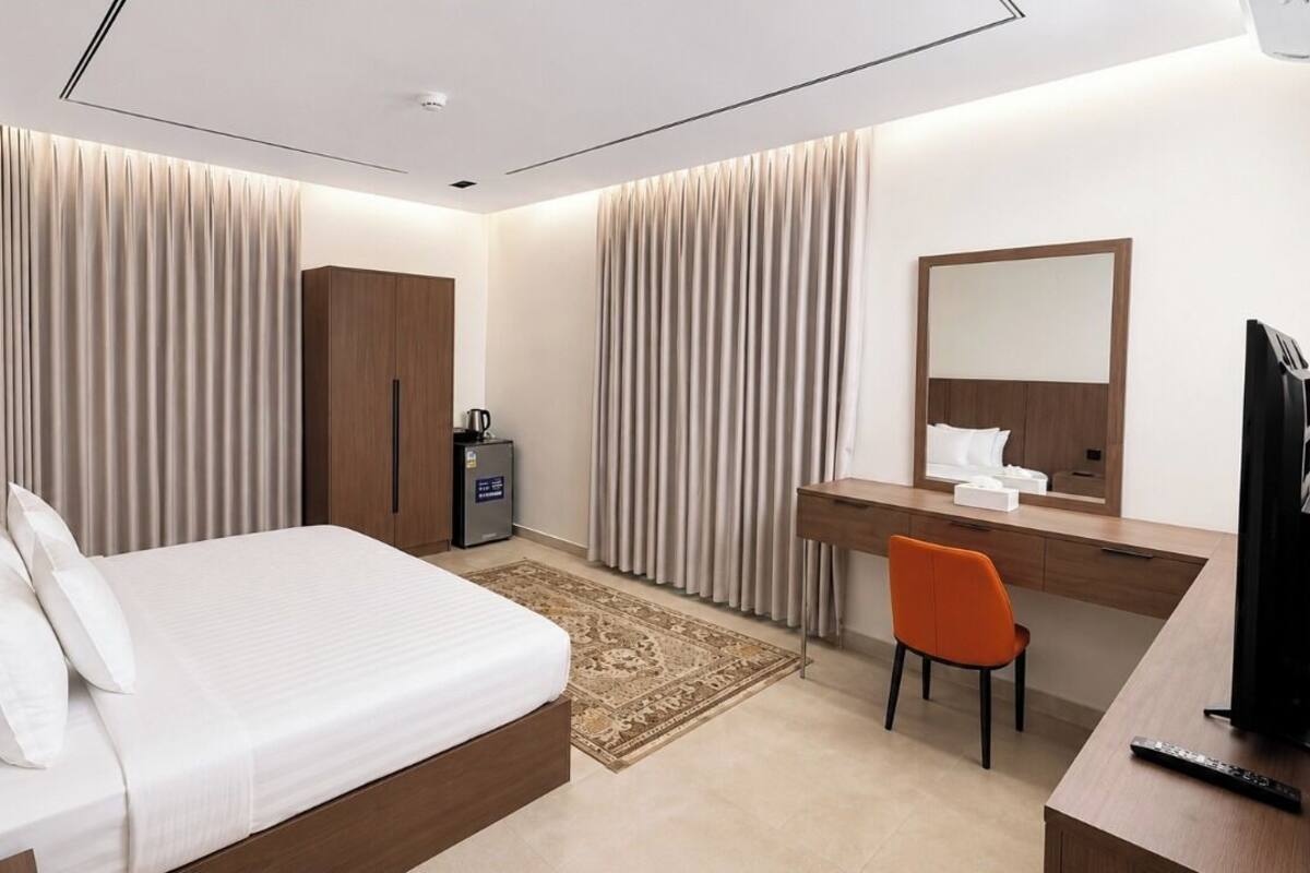 Una habitación de hotel con cama, escritorio, silla, espejo y televisión.