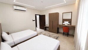 Habitación de hotel con dos camas, un escritorio, una silla, un armario, un espejo y aire acondicionado.