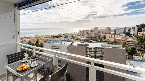 Ein Balkon mit Frühstückstisch, Blick auf eine Stadtlandschaft mit Gebäuden und Meer.