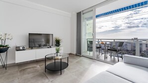 Ein modernes Wohnzimmer mit Fernseher, einem Glastisch, einer Couch und einem Balkon mit Blick auf die Stadt.