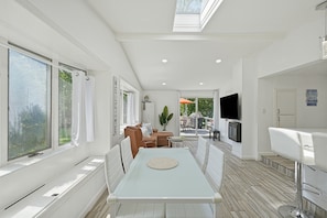 A modern kitchen with a dining area, large windows, and a TV.