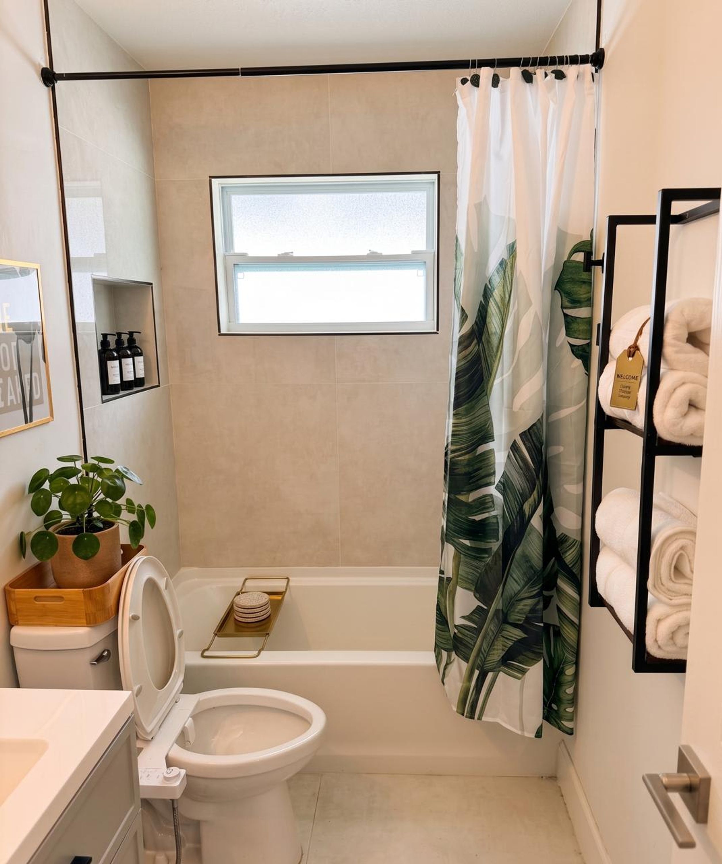 Baño con inodoro, ducha con cortina, ventana, repisa con artículos de aseo y toallero.