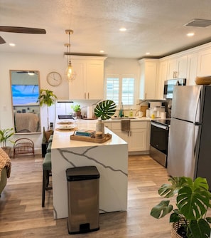 A modern kitchen with white cabinets, a marble island, stainless steel appliances, and a large window. - St Pete Retreat Game Room Outdoor Bar Sleeps 8 (St. Petersburg)